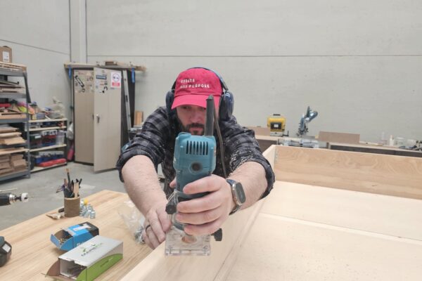 Carpintero utilizando una fresadora para mecanizar una pieza de madera durante la fabricación de un dormitorio a medida.