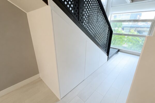 Armario bajo escalera fabricado a medida con puertas lisas lacadas en blanco e integración completa con la arquitectura de la vivienda.