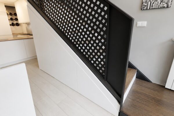 Armario integrado bajo escalera con puertas lisas lacadas en blanco, diseñado a medida para aprovechar el espacio sin romper la estética de la vivienda.