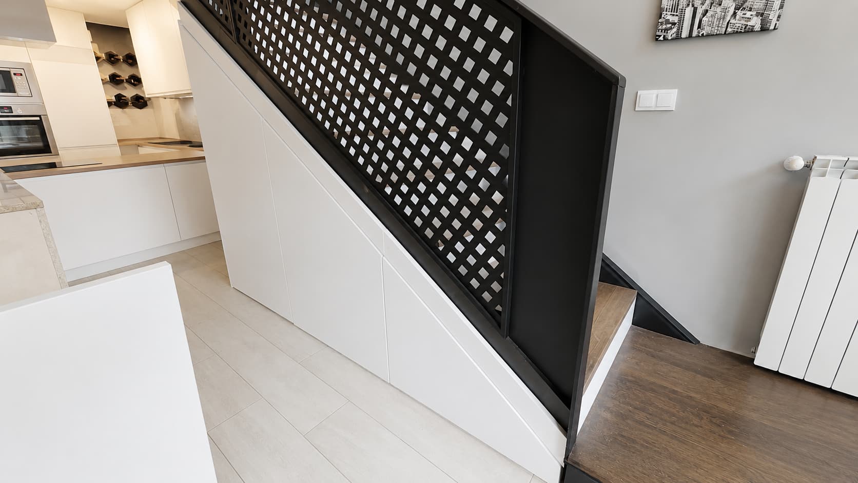 Armario integrado bajo escalera con puertas lisas lacadas en blanco, diseñado a medida para aprovechar el espacio sin romper la estética de la vivienda.