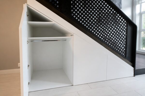 Interior de armario bajo escalera a medida con barra para colgar ropa, balda superior y compartimentos adaptados a la inclinación de la escalera.