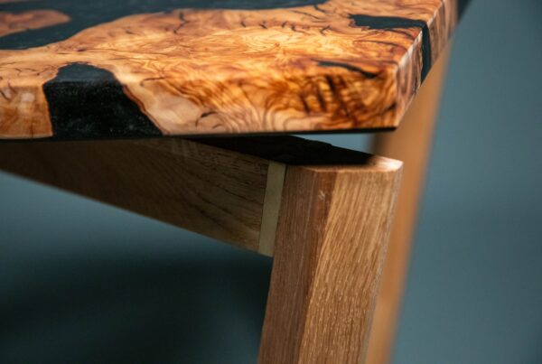 Primer plano del canto del tablero de una mesa de centro artesanal fabricada en madera de olivo y resina epoxi negra, apoyado sobre una estructura de roble macizo.