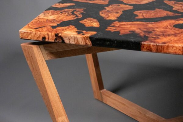 Detalle de la esquina de una mesa de centro artesanal con tablero de madera de olivo y resina epoxi negra sobre estructura de roble macizo.
