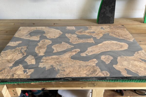 Tablero de mesa de centro fabricado con madera de olivo y resina epoxi negra después del mecanizado, listo para comenzar el proceso de lijado.