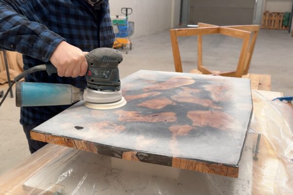 Lijado del tablero de una mesa de centro fabricada con madera de olivo y resina epoxi negra durante el proceso de acabado artesanal.