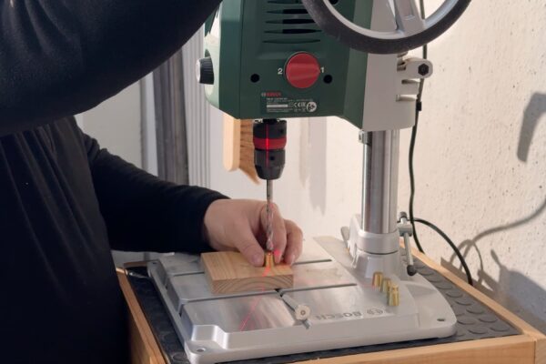 Taladrado de precisión para instalar insertos roscados de latón en la estructura de una mesa de centro artesanal de madera maciza.