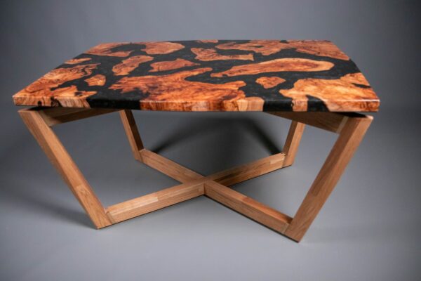 Vista frontal de una mesa de centro artesanal con tablero de madera de olivo y resina epoxi negra sobre una estructura geométrica de roble macizo.